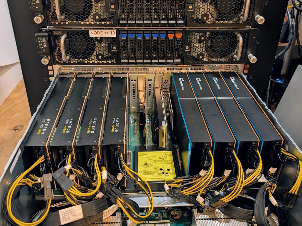 Baie informatique ouverte : deux nœuds de calcul Gigabyte au-dessus d’un châssis contenant huit cartes accélératrices AMD Radeon Instinct MI50 et Radeon Pro V520, reliées par des faisceaux de câbles d’alimentation jaunes.